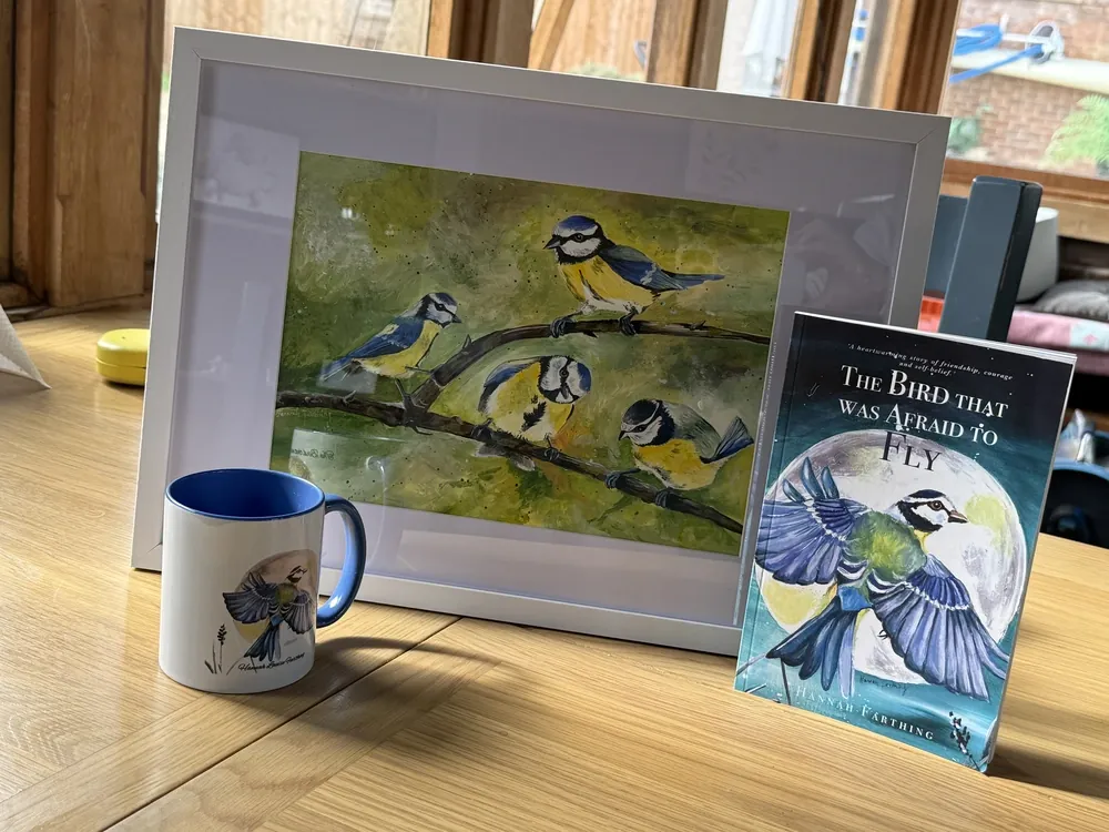 The framed Flock painting displayed with The Bird That Was Afraid to Fly book and mug.