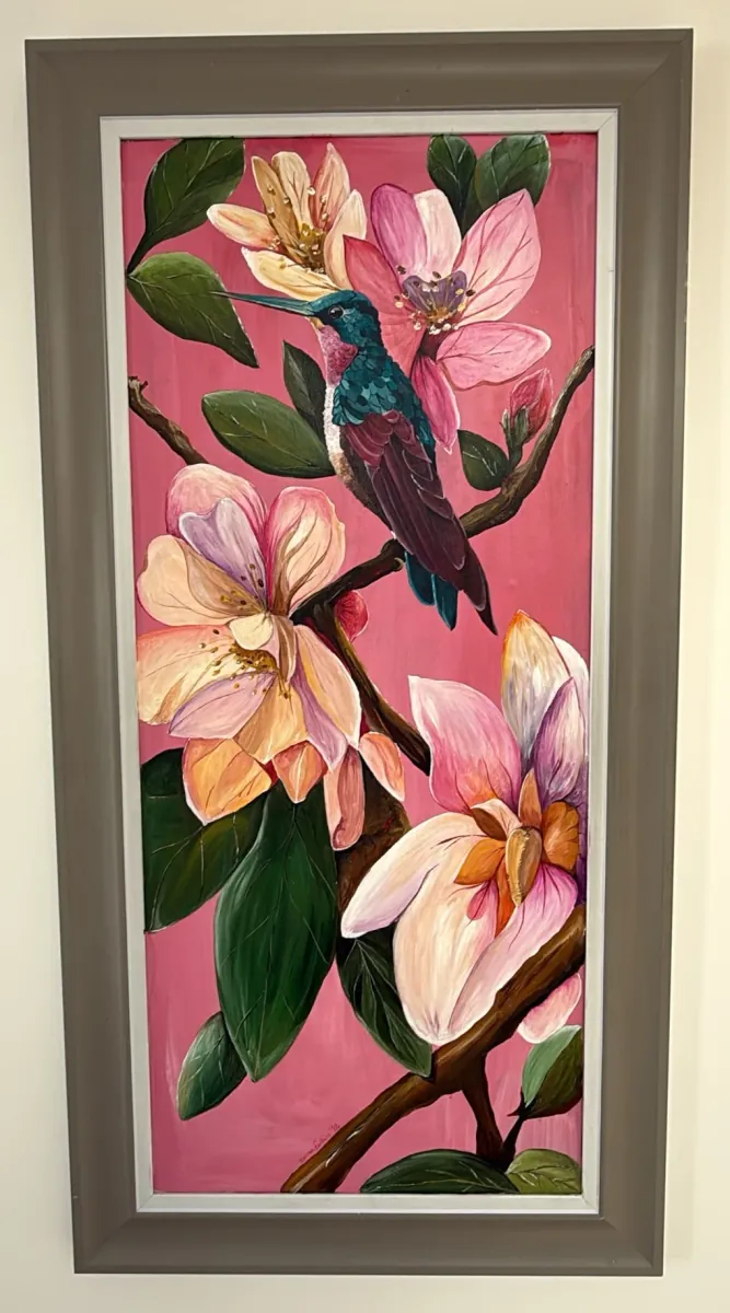 Hummingbird in Magnolia: acrylic painting of a green hummingbird among pink magnolia flowers, in a tall grey frame.