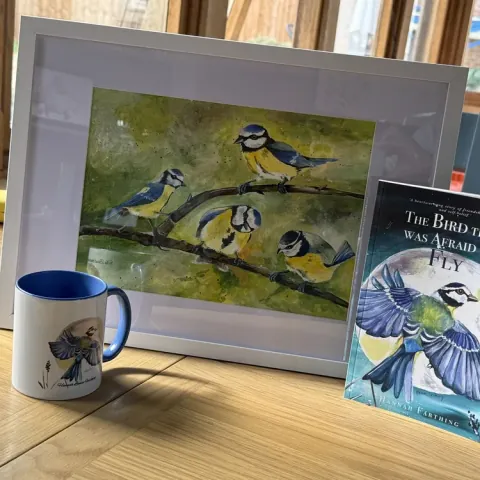 The framed Flock painting displayed with The Bird That Was Afraid to Fly book and mug.